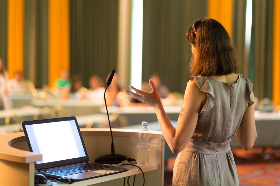 How to Choose the Best Conference Room Setup for Your Event 4 Conference room setup woman giving presentation from stage